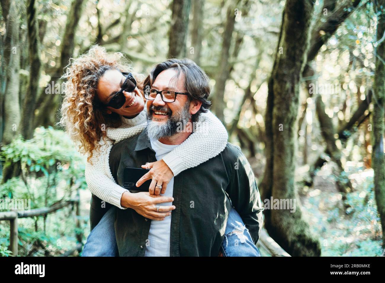 Ein glückliches Paar genießt gemeinsam Freizeitaktivitäten im Freien, trägt eine Frau im Huckepack und hat Spaß in der Beziehung. Freude Leute haben Spaß in der Natur Wald Wochenendreiseziel Stockfoto
