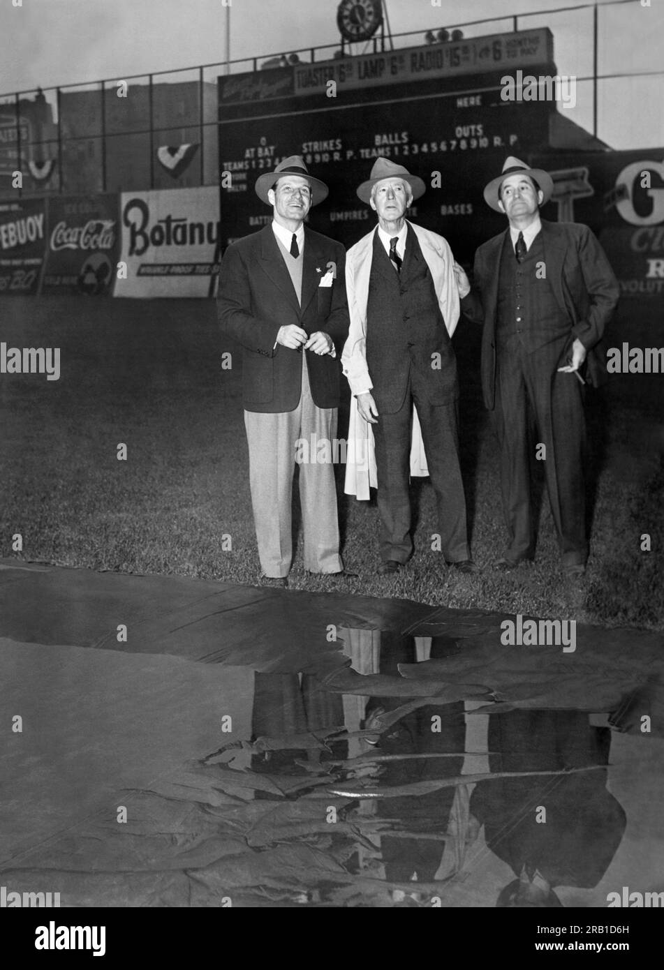 New York, New York: 3. Oktober 1941 Brooklyn Dodger Manager Leo Durocher, Baseball Commissioner Kenesaw Landis und New York Yankee Manager Joe McCarthy stehen am Rand der Infield-Plane und werfen die Augen auf den dunklen Himmel, der das World Series Game 3 der „U-Bahn“ auf dem Ebbets Field in Brooklyn verschoben hat. Stockfoto