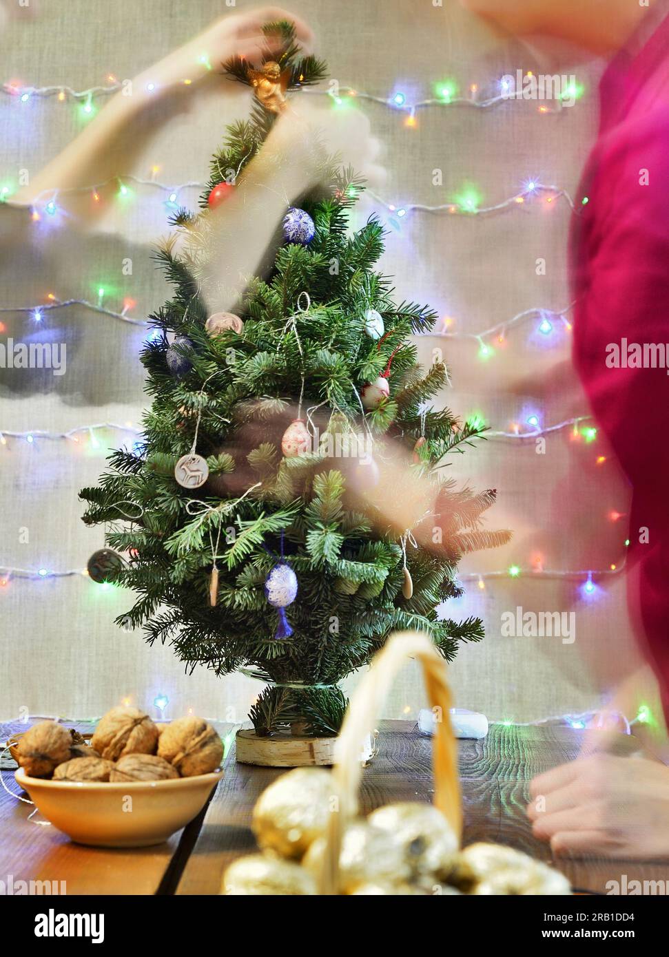 Festlich dekorierter grüner Weihnachtsbaum mit brennenden Kerzen und verschwommener Beleuchtung der Hände Stockfoto