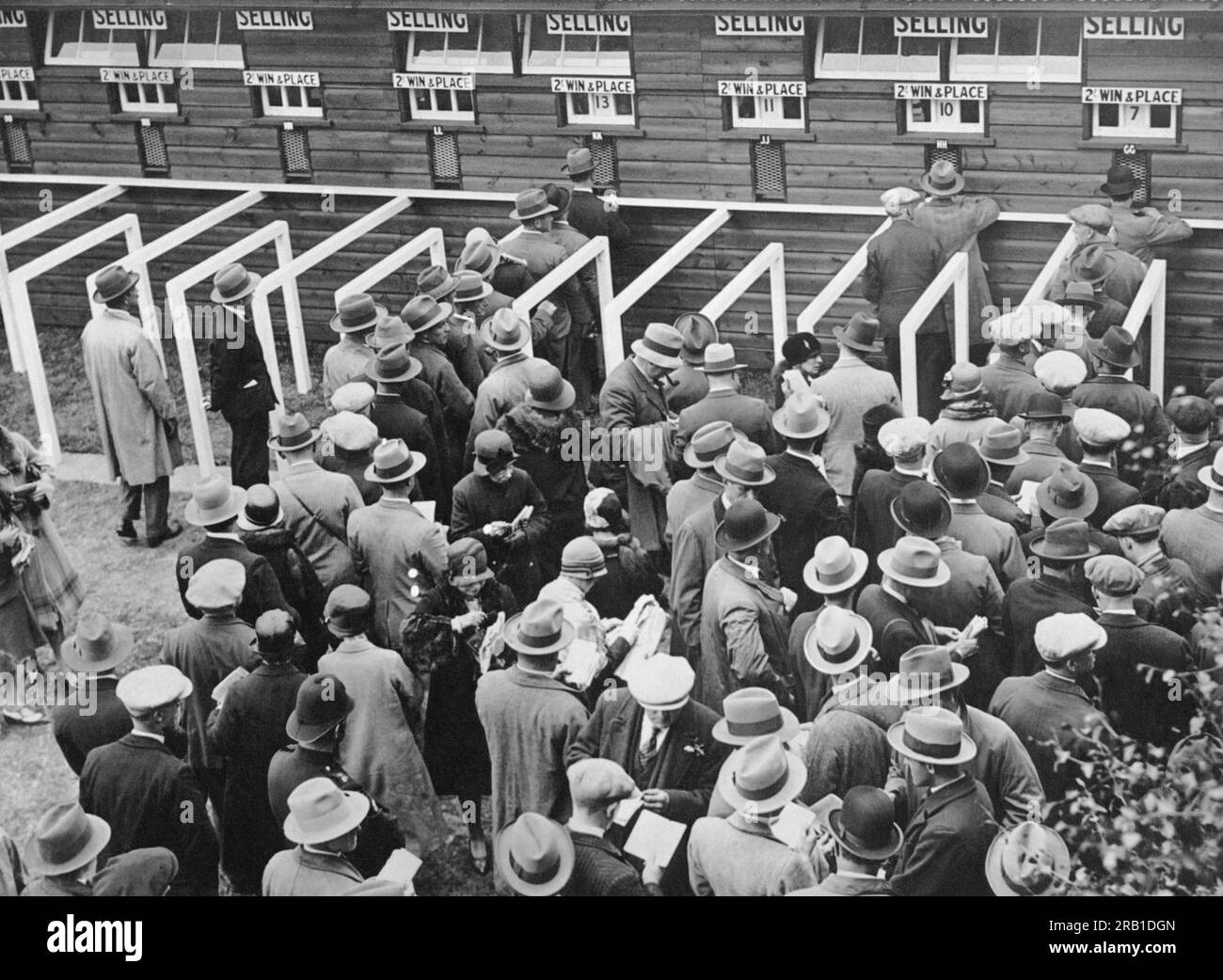 England: c. 1932 Pferderennsport-Fans stellen sich in Schlange, um ihre Wetten an den Ticketschaltern zu platzieren. Stockfoto