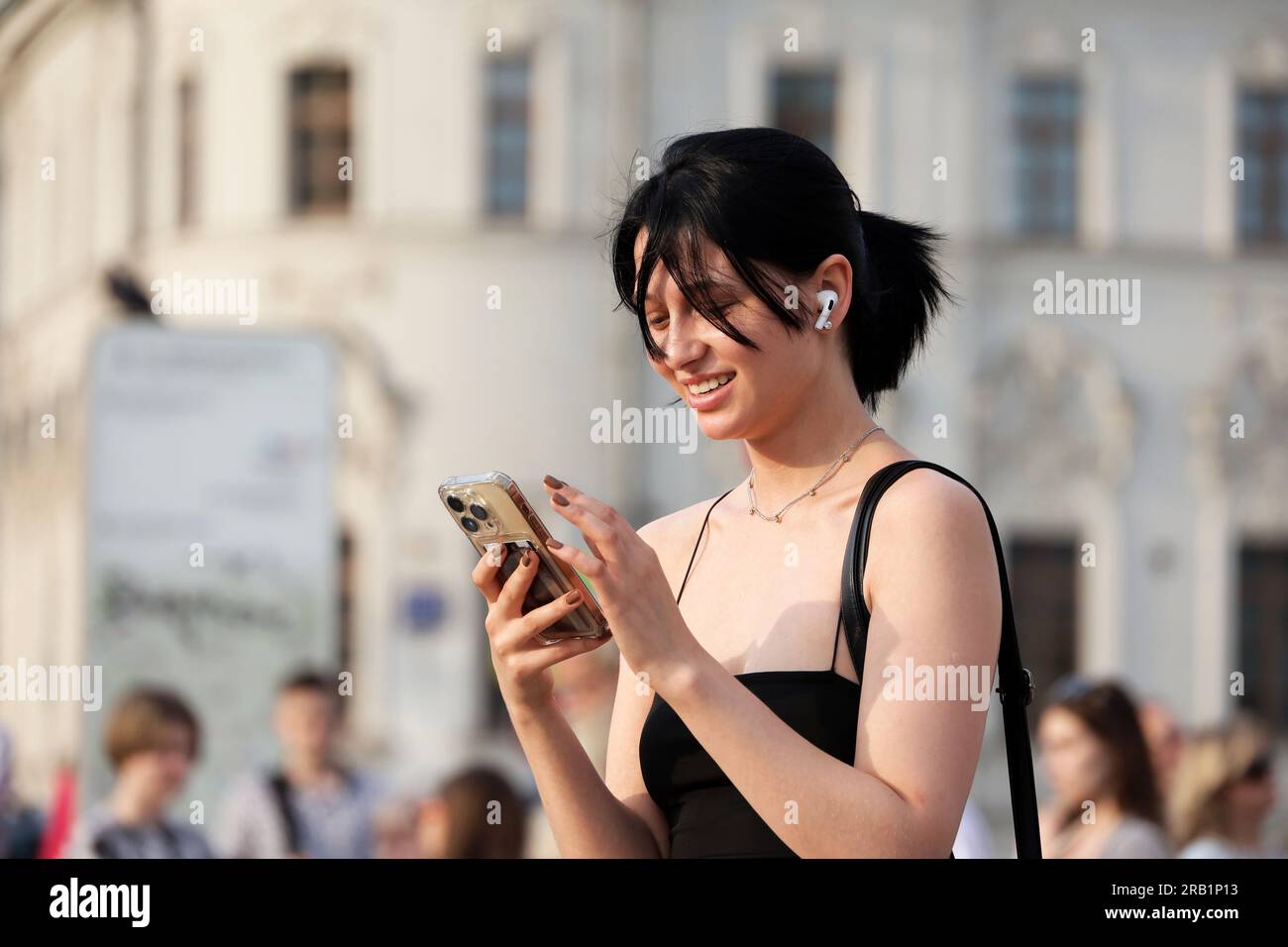 Glückliches Mädchen, das in der Sommerstadt ein Handy benutzt, Smartphone in weiblicher Hand Stockfoto