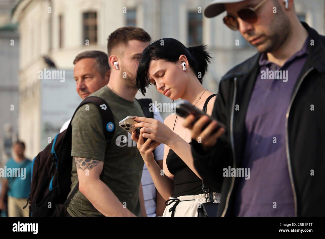 Menschen, die in der Sommerstadt Mobiltelefone benutzen, hübsches Mädchen mit Smartphone in der Hand im Vordergrund Stockfoto