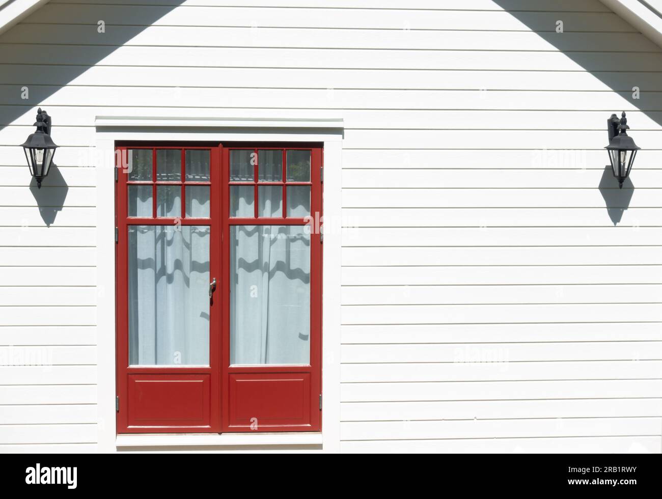 Rote gerahmte Glastür aus kleinem Holzschuppen mit leerer Wand aus weiß lackierten horizontalen Brettern Stockfoto