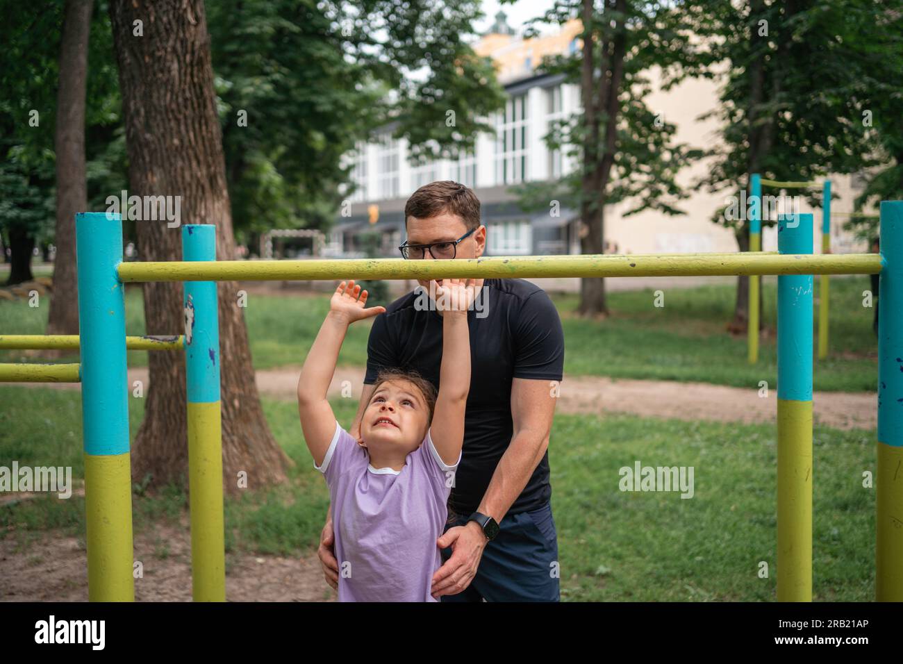 Vater mit Kind, das auf dem Outdoor-Fitnessbereich Pull-ups macht. Gesunder, aktiver Lebensstil, glückliche Familienzeit. Modernes Vaterschaftskonzept Stockfoto