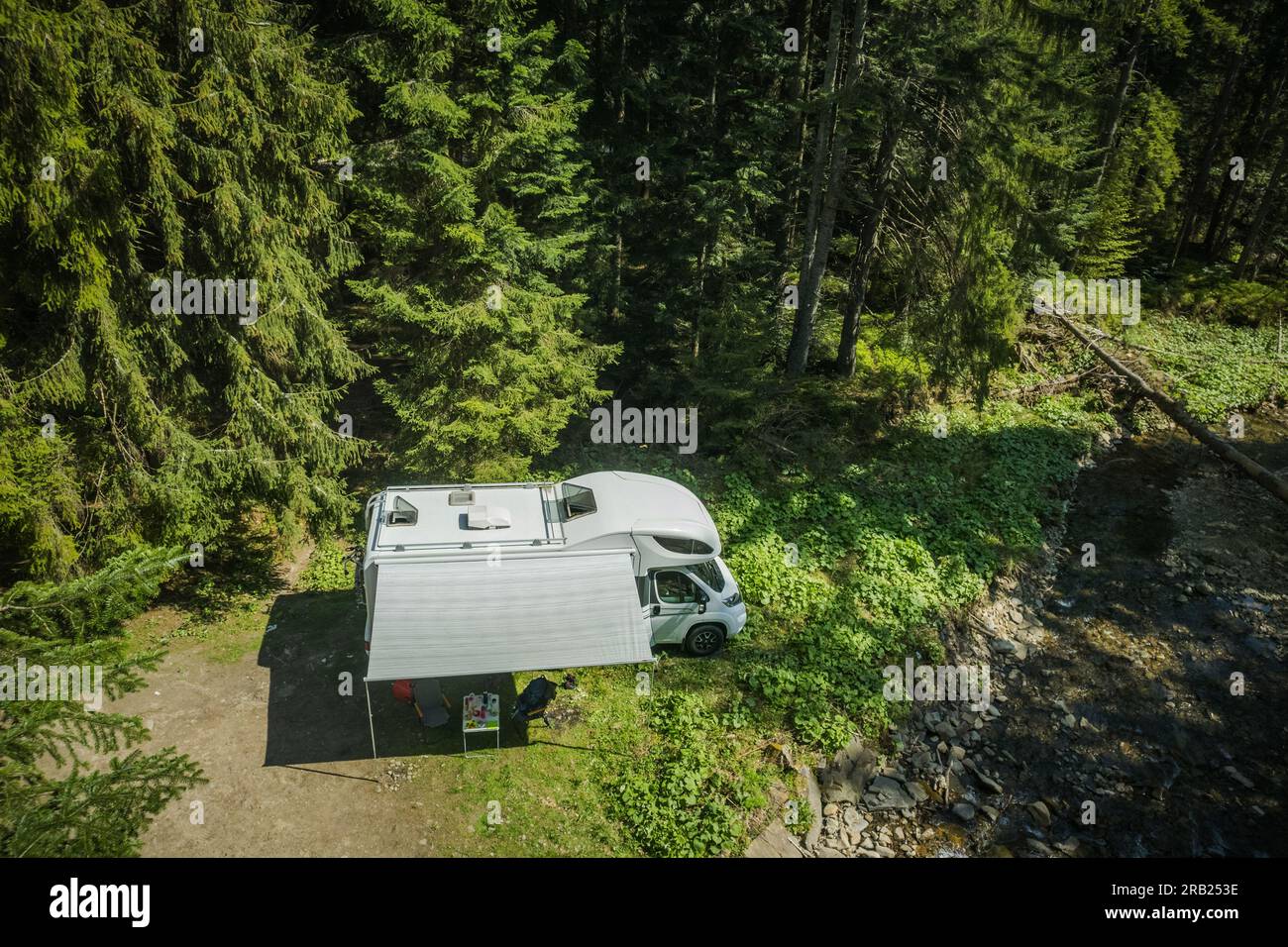 Blick aus der Vogelperspektive auf den weißen Camper Van, der im Wald neben dem Waldstrom parkt. Wohnmobil-Camping- und Reisemöglichkeiten. Stockfoto