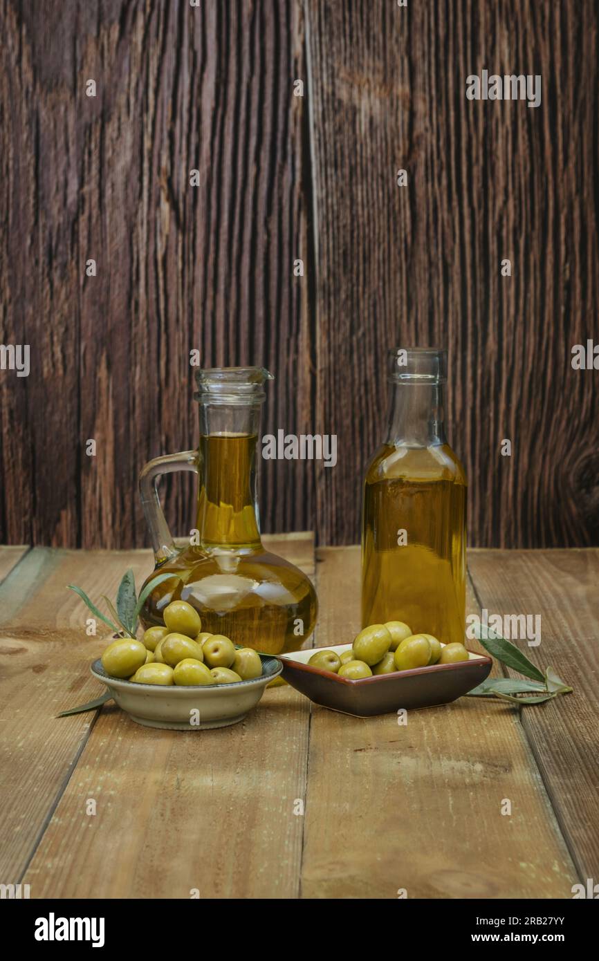 Stillleben mit zwei Glasbehältern gefüllt mit nativem Olivenöl zusammen mit einigen Tellern mit Oliven Stockfoto