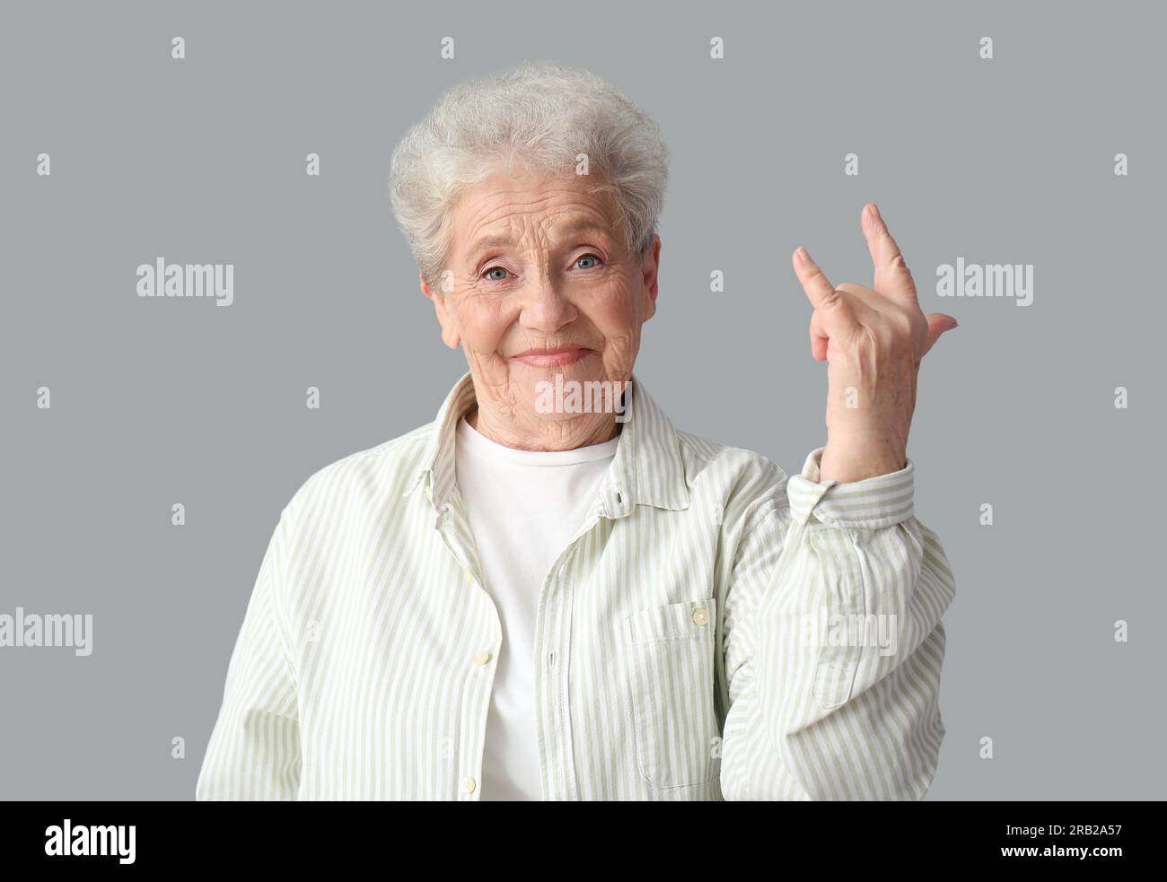 Seniorin zeigt Geste "ich liebe dich" auf grauem Hintergrund Stockfoto