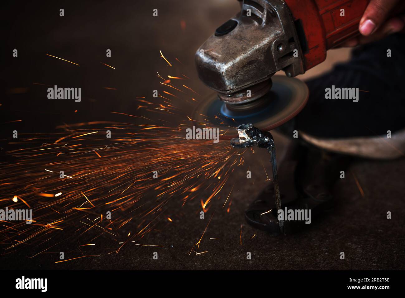 Arbeiter, der Stahl mit einem handlichen elektrischen Schleifgerät schneidet Stockfoto