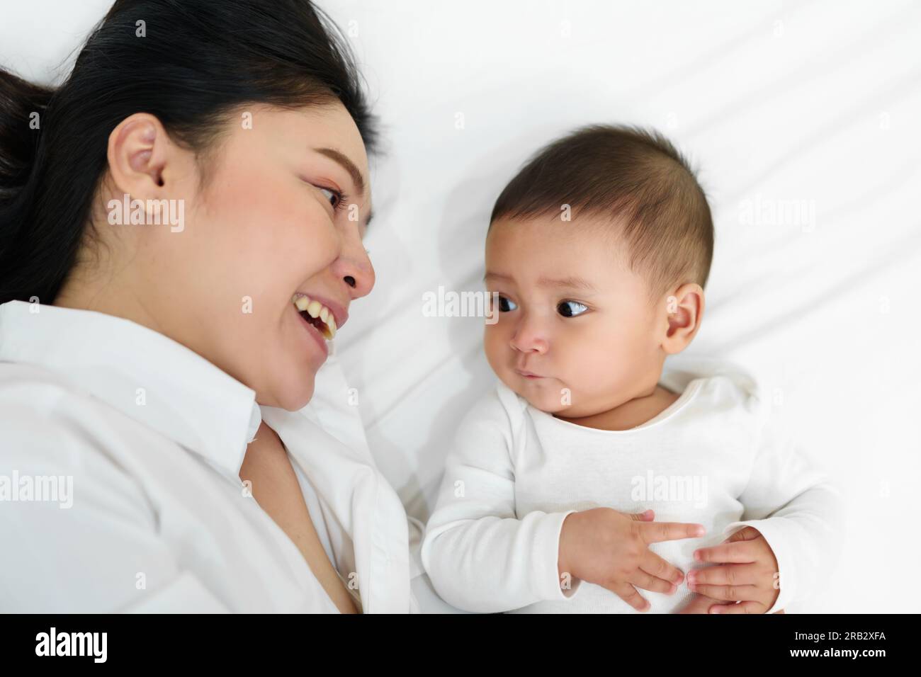 Glückliche Mutter, die mit ihrem Baby auf einem Bett liegt (Draufsicht) Stockfoto