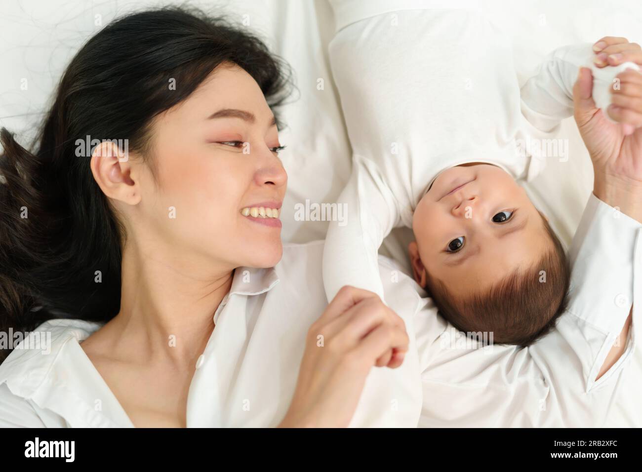 Glückliche Mutter, die mit ihrem Baby auf einem Bett spielte und lag (Draufsicht) Stockfoto