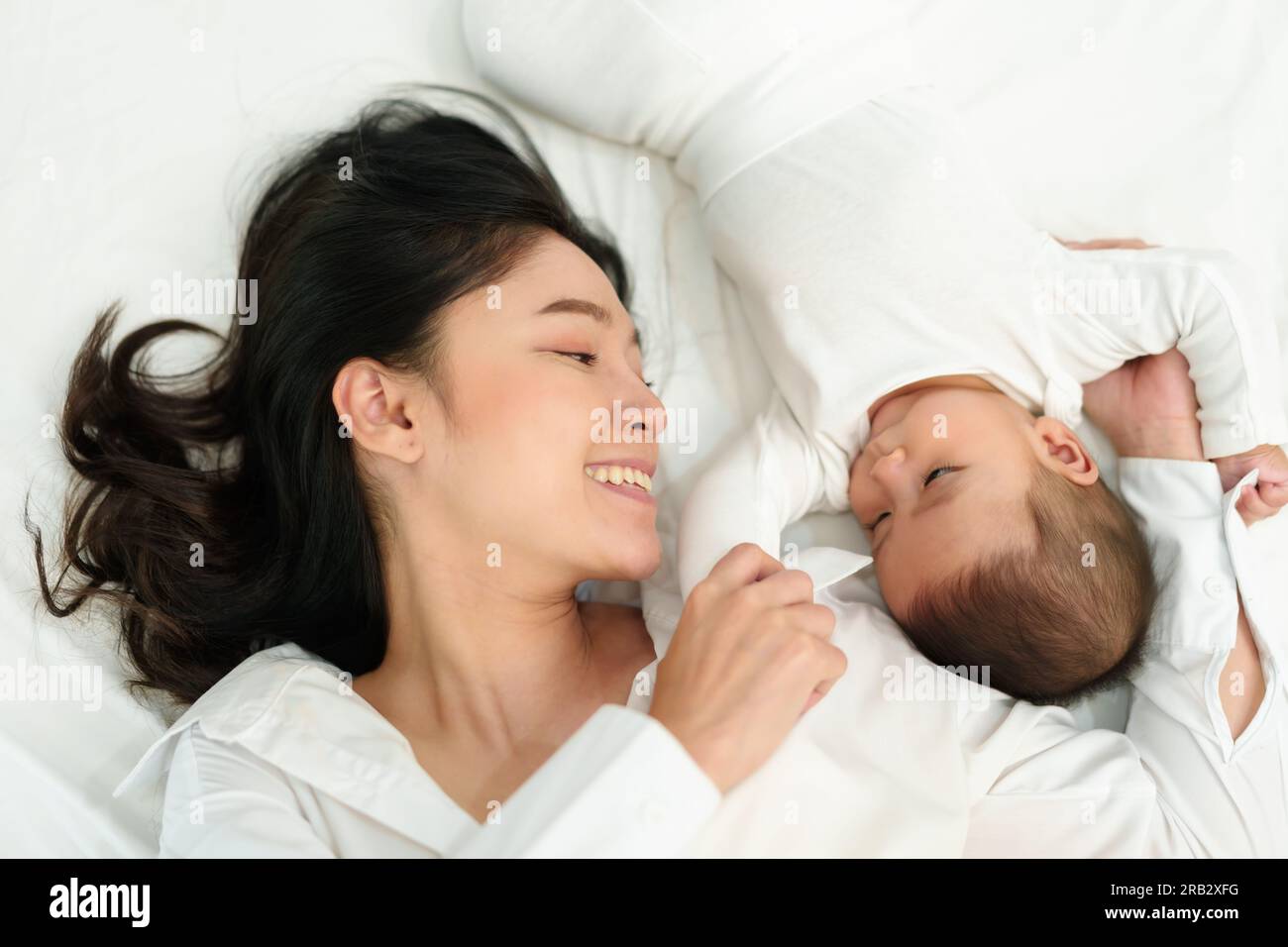 Glückliche Mutter, die mit ihrem Baby auf einem Bett spielte und lag (Draufsicht) Stockfoto
