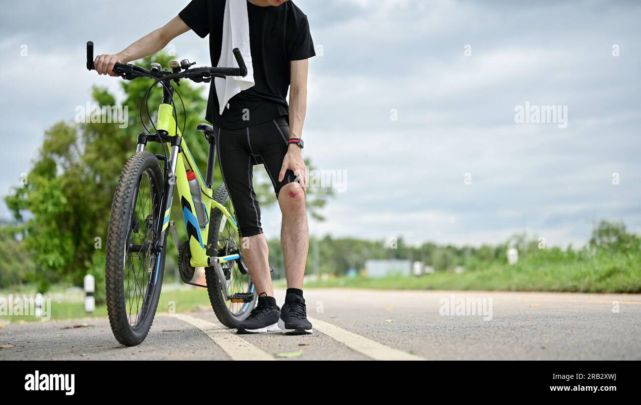 Abgeschnittenes Bild eines verletzten männlichen Radfahrers, der mit seinem Fahrrad auf der Straße spaziert. Knieschmerzen, vom Fahrrad gefallen, Unfall beim Radfahren Stockfoto