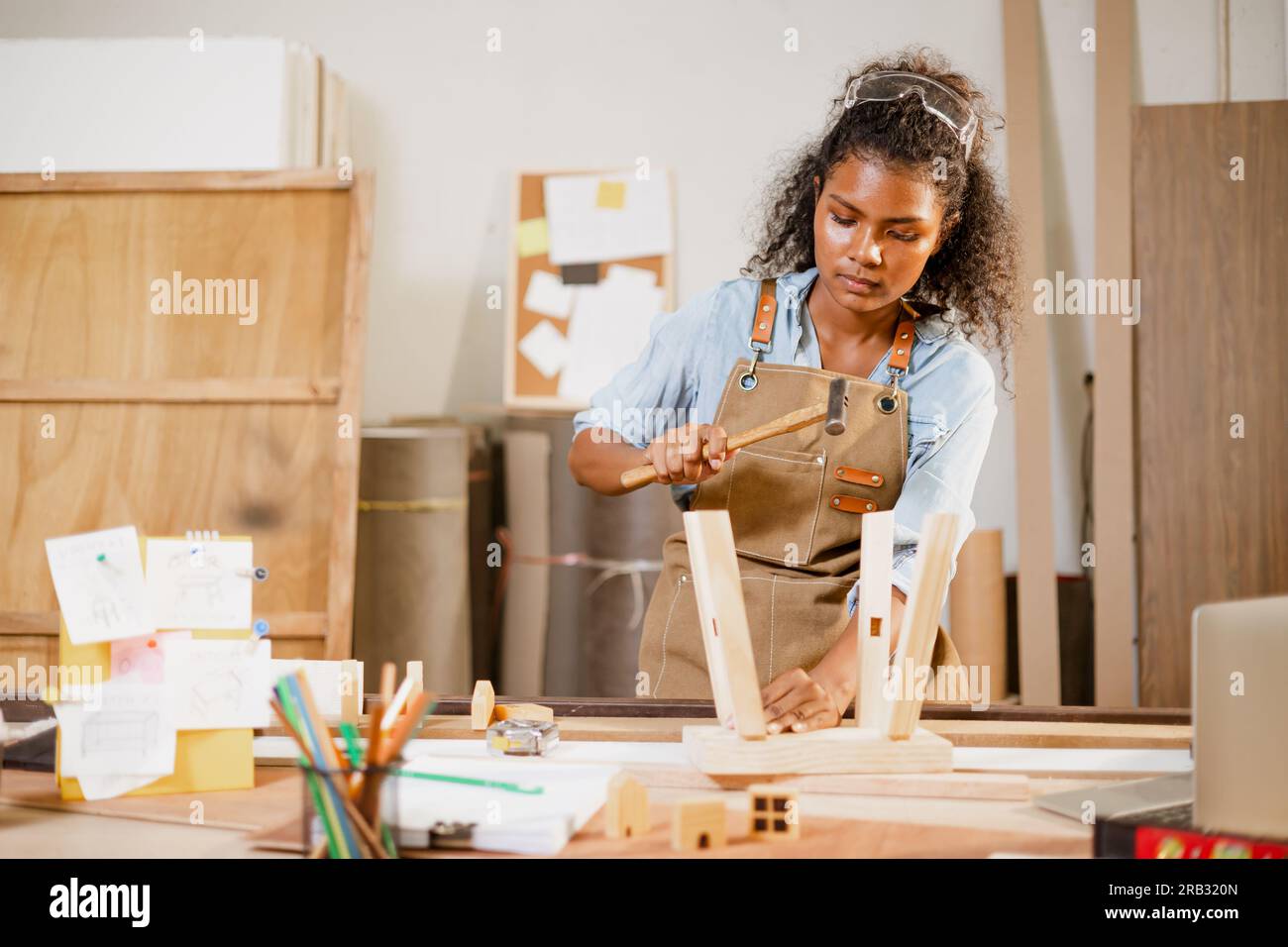 Afrikanische schwarze Schreinerin, die arbeitet, baut Holzstühle, handgefertigte Möbel in einer Studiowerkstatt aus Holz. Stockfoto