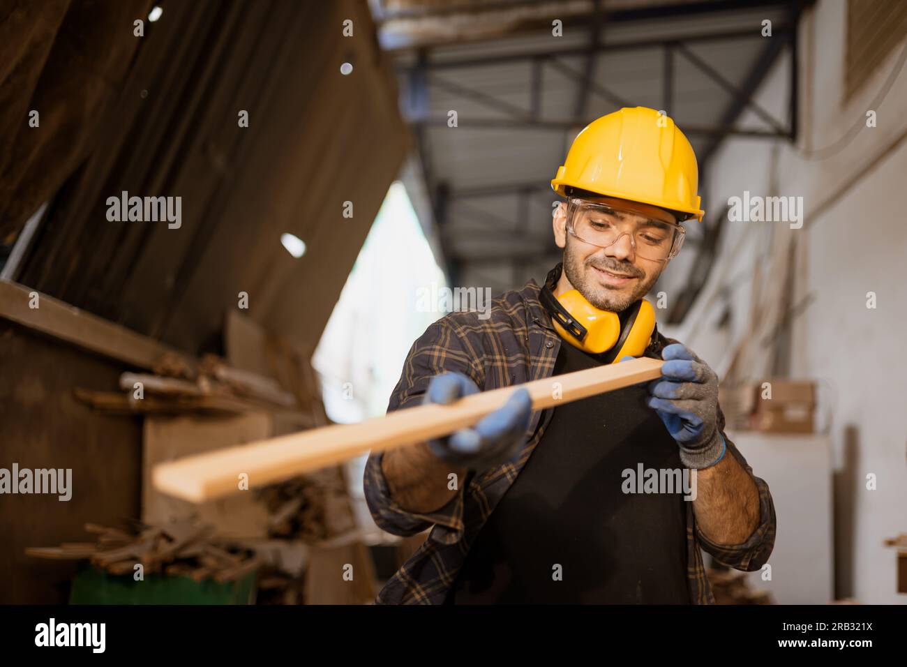 Glücklicher Zimmermann, der arbeitet, schaut sich das Material von Holzplatten an, um meisterhafte Holzmöbel herzustellen. Stockfoto
