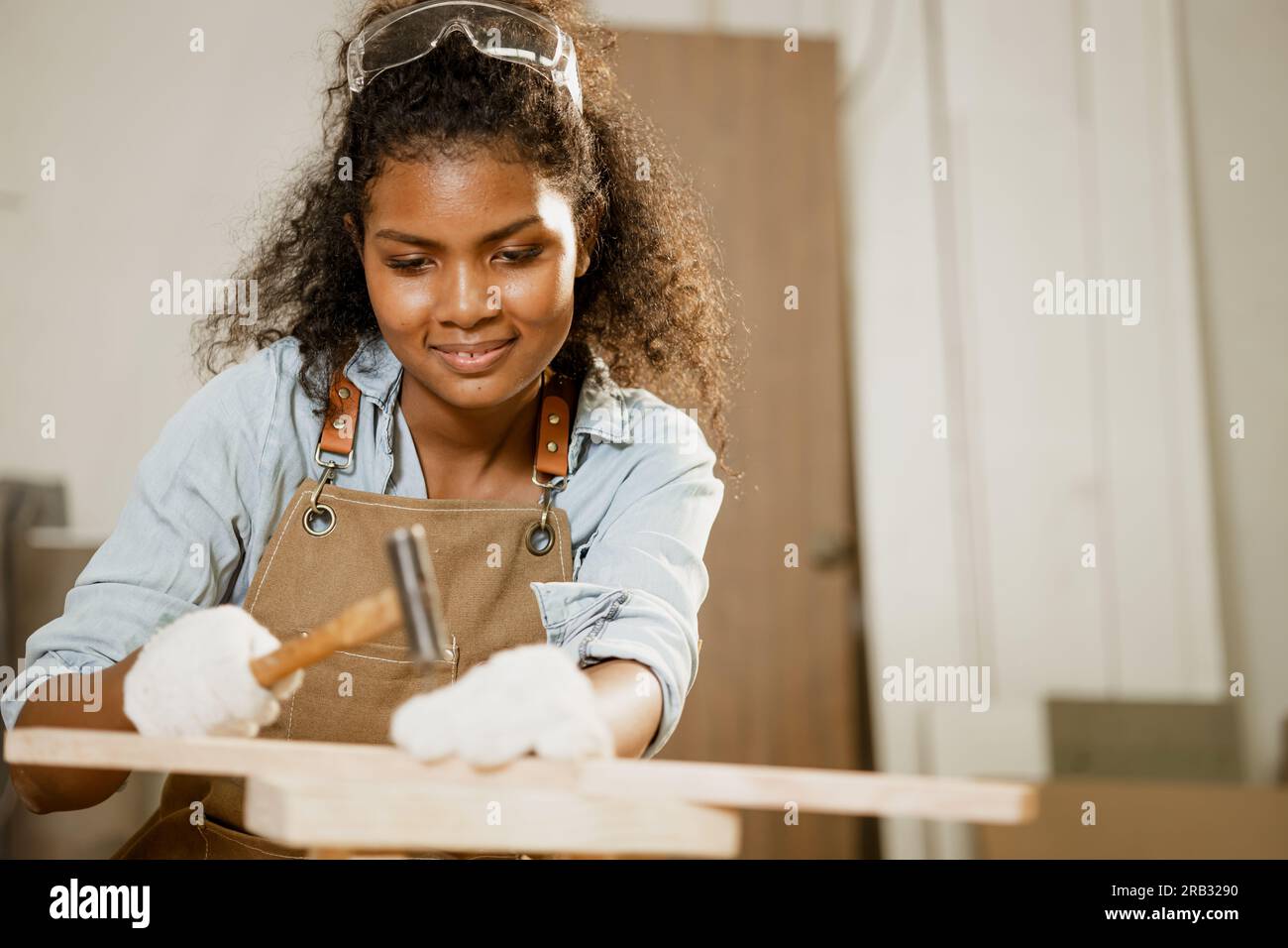 Schlaue glückliche Frau Holz Arbeitshammer auf Holzbrett Projekt Heimmöbel heimwerker in der Werkstatt. Stockfoto