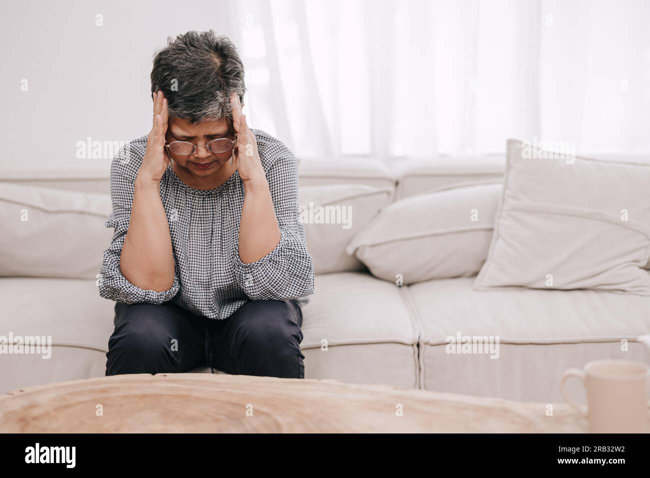 Reife Erwachsene asiatische Frau sitzende Hände bedecken Kopf fühlen sich schlecht Stress Kopfschmerzen denken ängstliche psychische Probleme. Ältere Hirnschmerzen leiden zu Hause Stockfoto