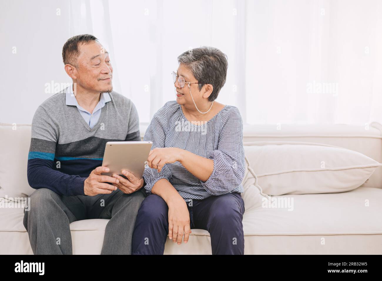 Glückliches Seniorenpaar genießt Technologie zusammen auf dem Heimsofa. Tablet für ältere Ehepaare stärken die familiären Bindungen mit moderner Technologie.Tech savvy husb Stockfoto