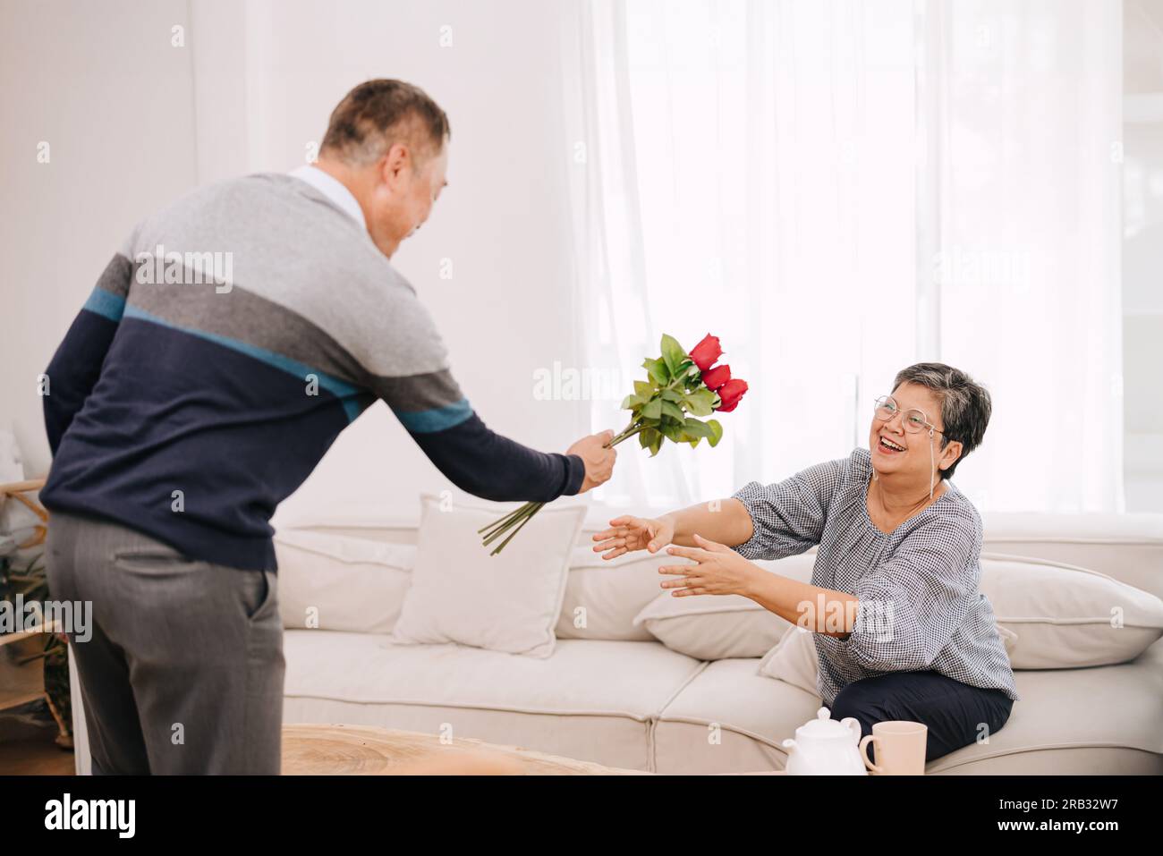 Seniorenpaar-Liebhaber niedlich sanfter Mann Überraschung, die seiner Frau zu Hause Rosen zum Hochzeitstag oder valentinstag schenkt Stockfoto