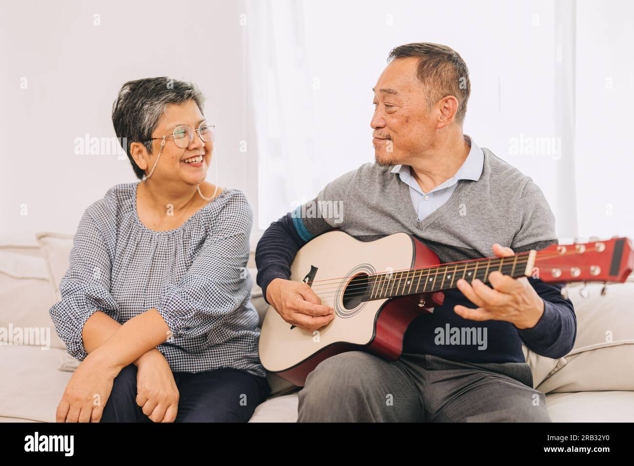 Seniorenpaar Liebhaber Urlaub zu Hause Aktivitäten Alter Mann spielt Gitarrenmusik macht ältere Frau glücklich lächeln Stockfoto