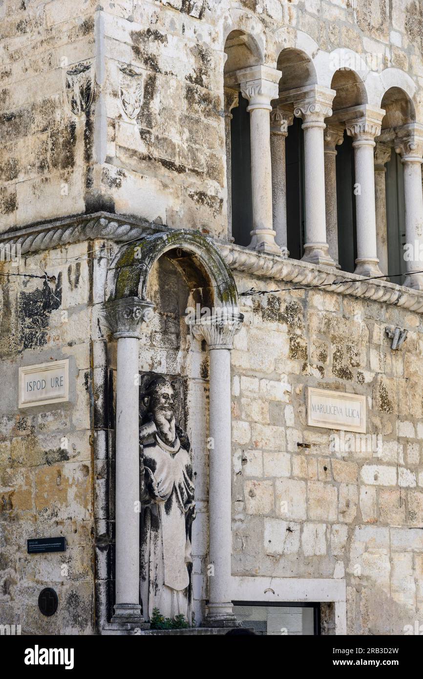 Eine Skulptur des Heiligen Antonius, des Eremitts, mit einem spät romanischen, gemusterten Fenster oben auf dem Ciprianis-Benedetti-Palast in Narodni Trg, Split, Dalmatien Stockfoto
