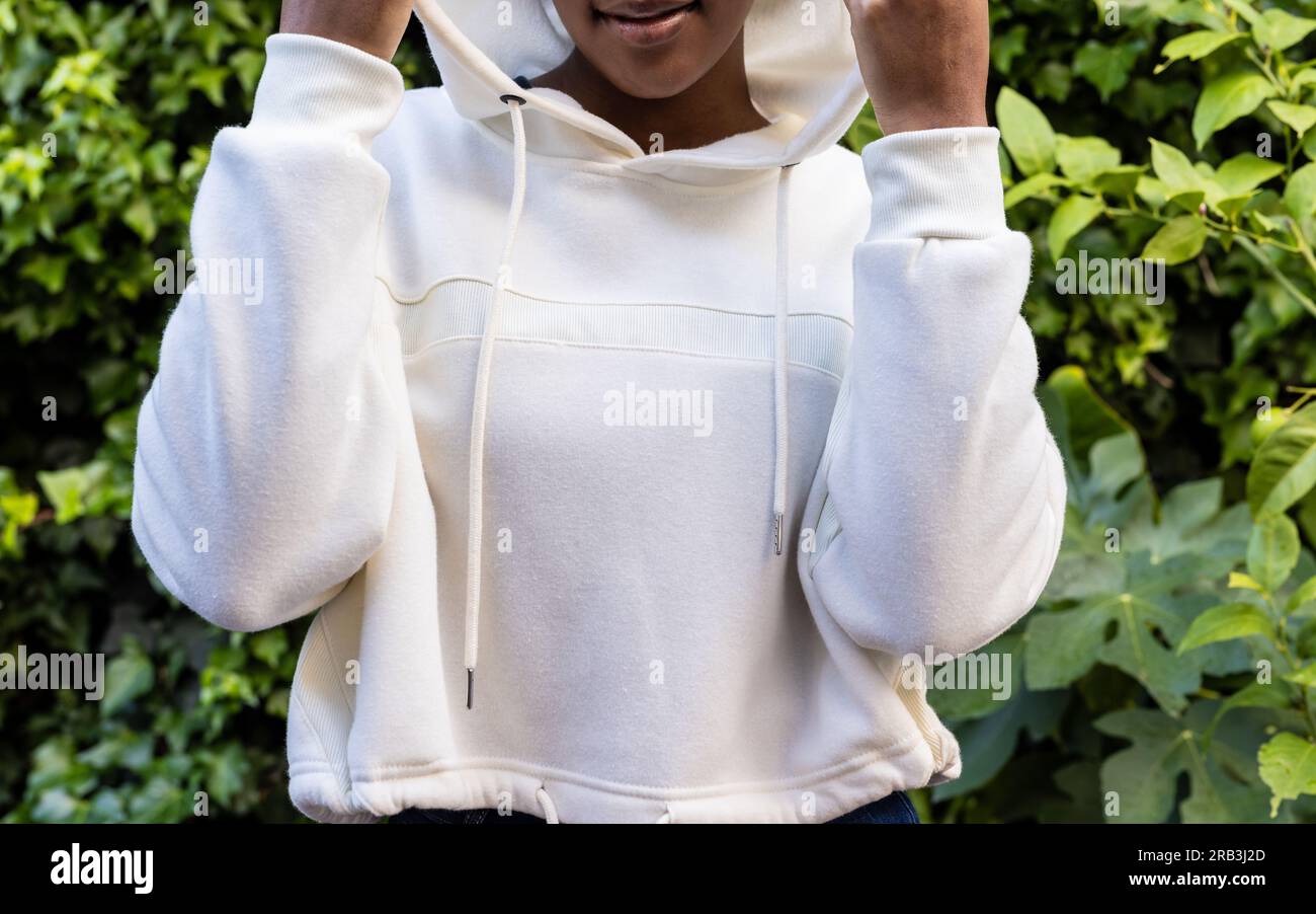 Eine afroamerikanerin, die im Garten ein weißes Kapuzenpullover trägt. Mode, Freizeitkleidung und Freizeitkleidung, unverändert. Stockfoto