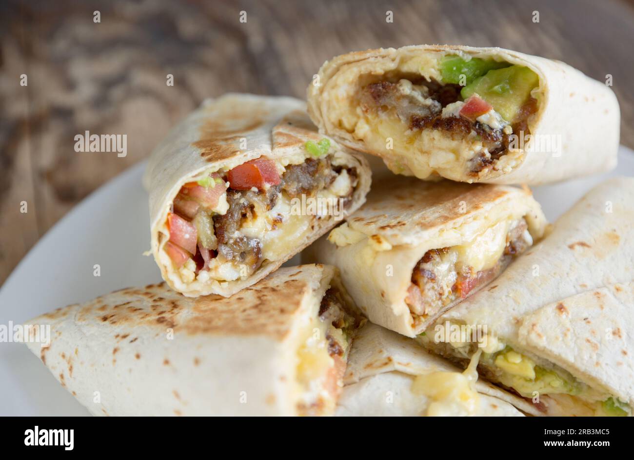 Ein hausgemachter Frühstücks-Burrito mit Avocado, Tomaten, gebratener Kartoffel, Speck, Käse und Rührei, verpackt in einer Tortilla. England GB Stockfoto