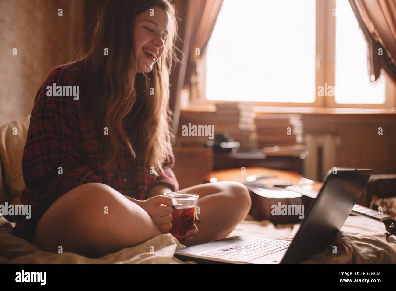 Glückliches Teenager-Mädchen mit einer Tasse Tee, das vor dem Laptop saß Stockfoto