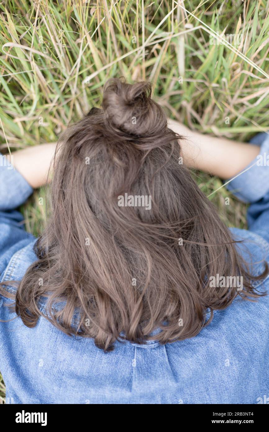 Brünette Frau mit Kopf in den Händen im Gras - Hinterkopf Stockfoto