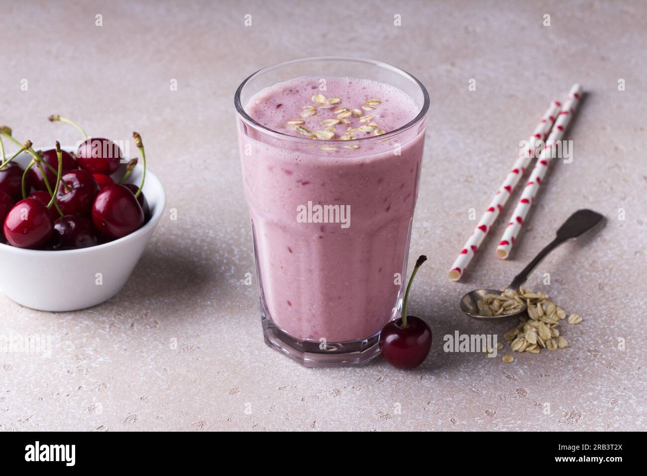 Milchshake mit Kirschen, Joghurt und Haferbrei, Trinkhalme, Schüssel mit frischen Kirschen auf einem beigen strukturierten Hintergrund Stockfoto