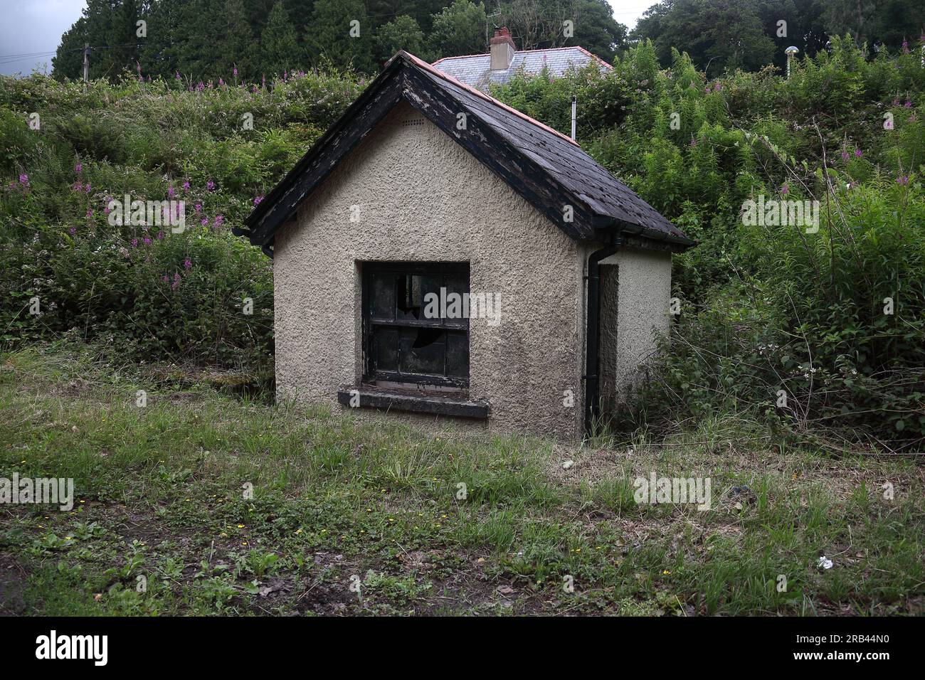Ein kleines versenktes Gebäude mit zwei Fenstern und einer Tür am Straßenrand in einem kleinen Dorf, dessen Nutzung unbekannt ist. Stockfoto