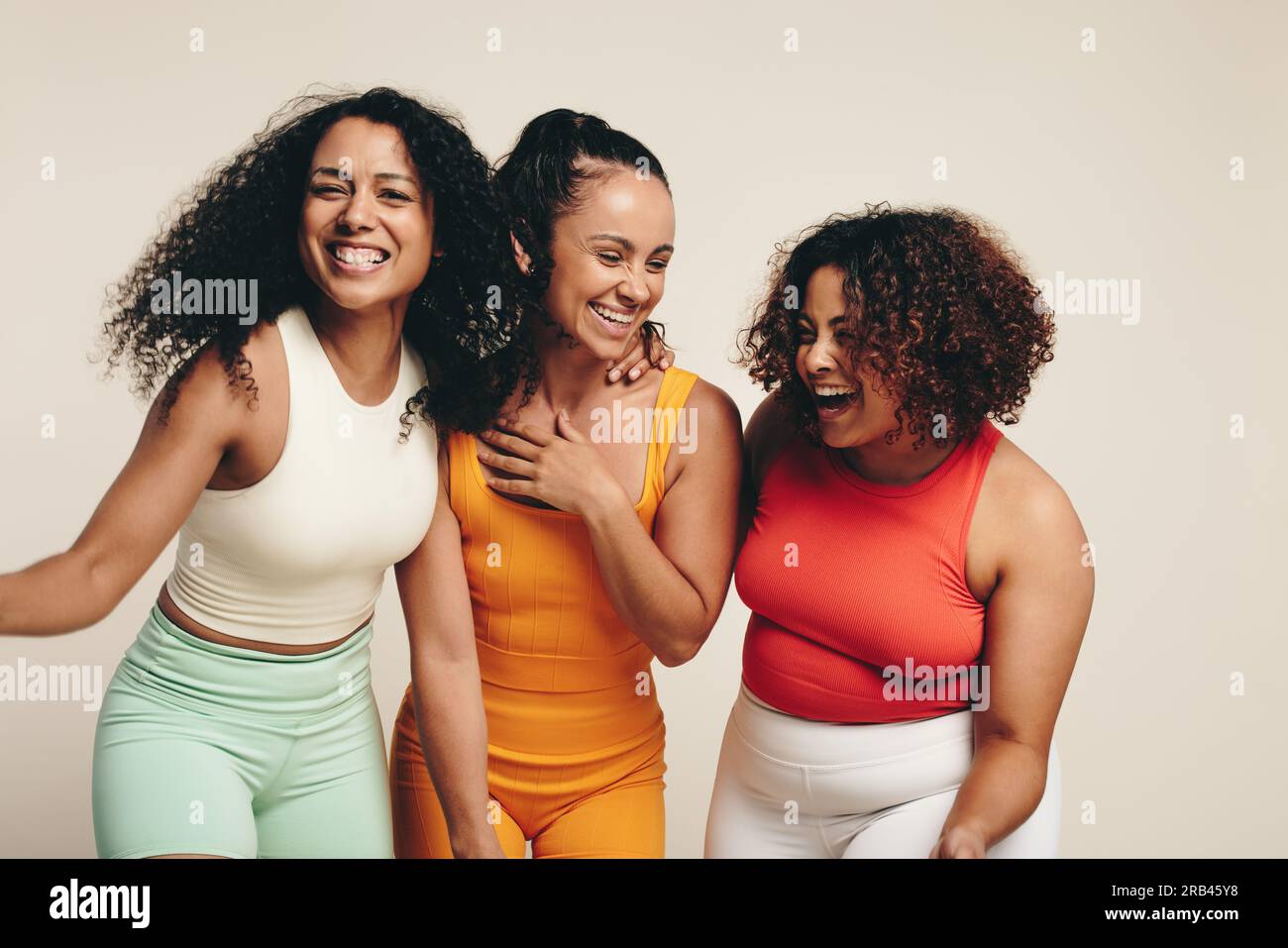 Eine Gruppe verschiedener junger Sportlerinnen lächelt und lacht, während sie im Studio in Sportbekleidung zusammen stehen und ihre feiern Stockfoto