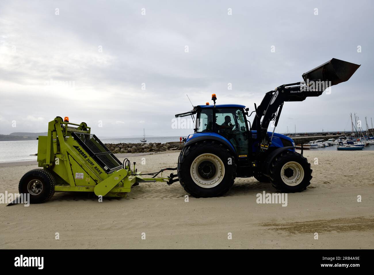Traktor zieht den Barber Surf Rake, um den Sand zu ebnen und den Strand Lyme Regis Dorset England zu reinigen Stockfoto