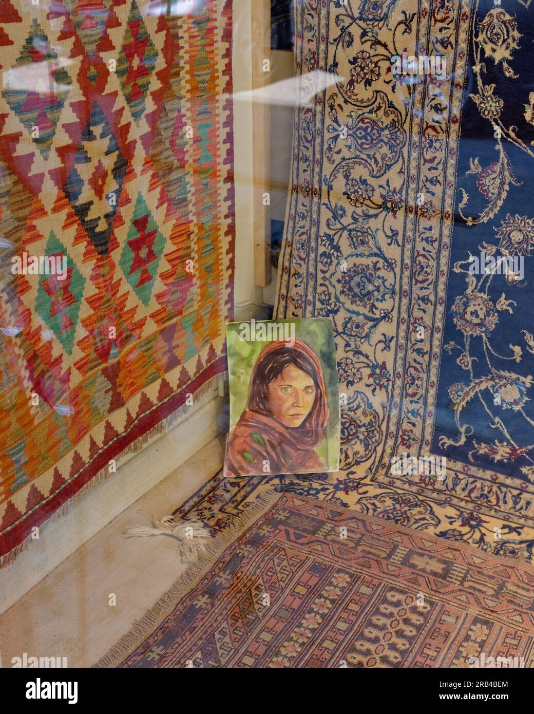 Teppiche in einem Schaufenster in Istanbul mit einem Gemälde des berühmten afghanischen Mädchens von Steve McCurry Stockfoto