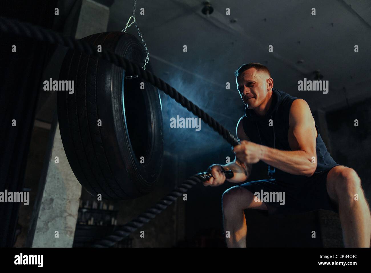 Kräftiger Muskelmann, der in einem dunklen Fitnessstudio mit Kampfseilen trainiert. Seile für Crossfit- und Crossfit-Übungen. Trainingshänder mit Kampfseilen. Hintergrundbeleuchtung. Stockfoto