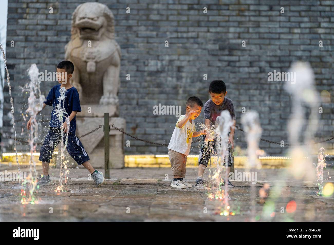 HEFEI, CHINA - 7. JULI 2023 - Kinder spielen mit Wasser, um sich an einem Brunnen auf einem Platz in Hefei, Provinz Anhui, China, abzukühlen, 7. Juli 2023. Stockfoto