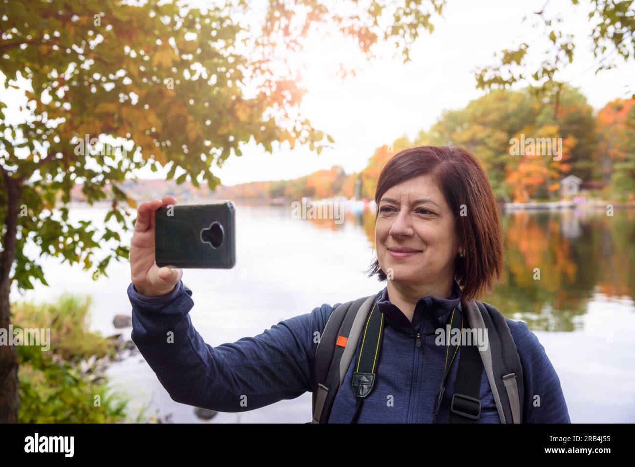 Brünette Touristen machen im Herbst ein Selfie am Ufer eines Sees Stockfoto