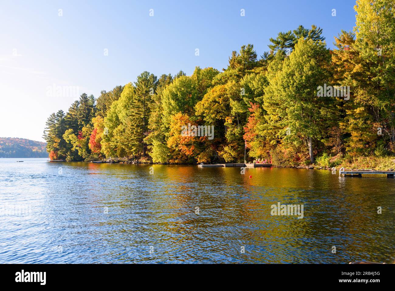 Farbenfrohe bewaldete Ufer eines Sees, der im Herbst von der untergehenden Sonne erleuchtet wird Stockfoto