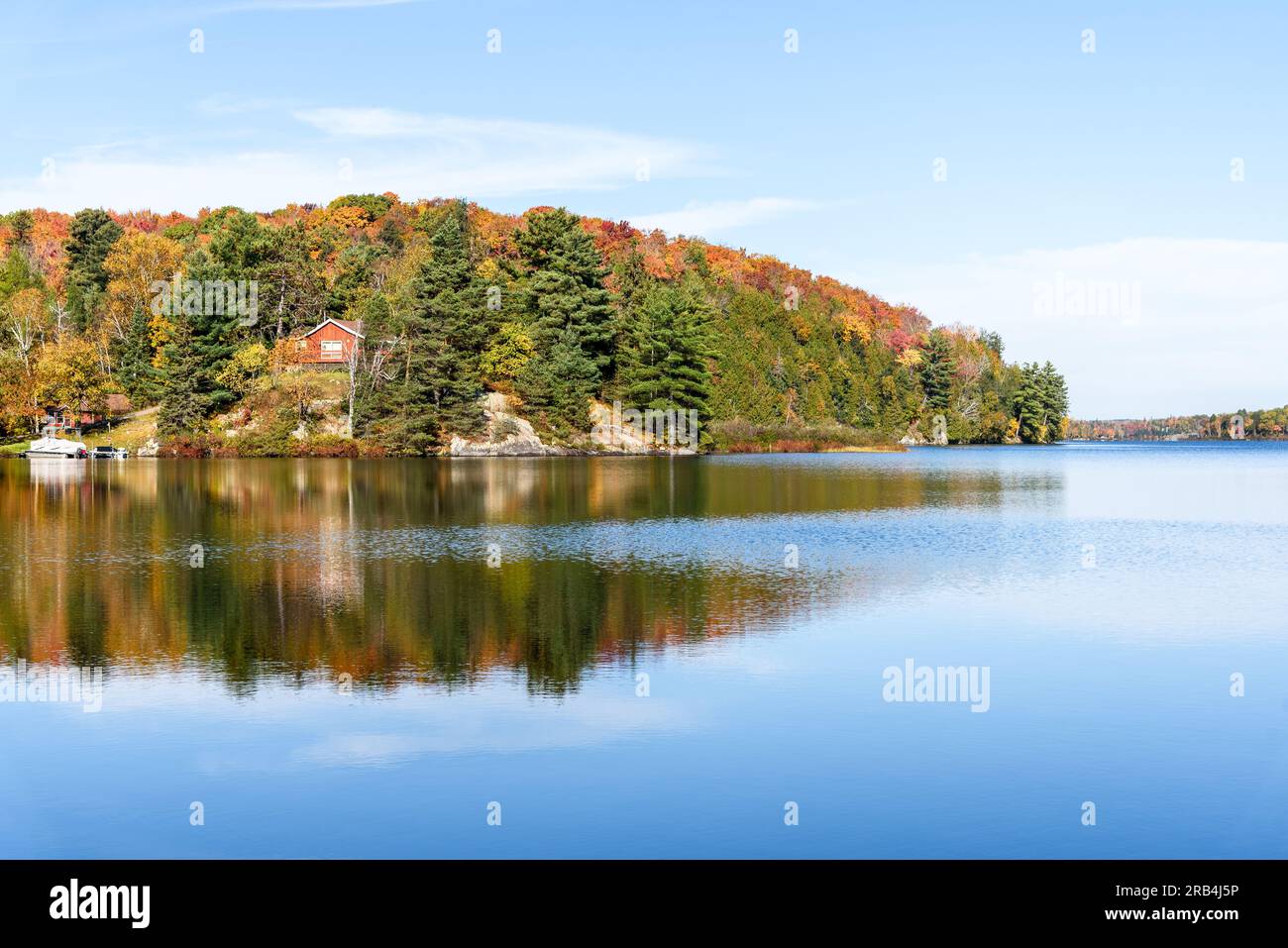 Häuser inmitten bunter Bäume auf dem Gipfel der Herbstkaoluren entlang des Ufers eines Sees auf einer klaren Brandung Stockfoto