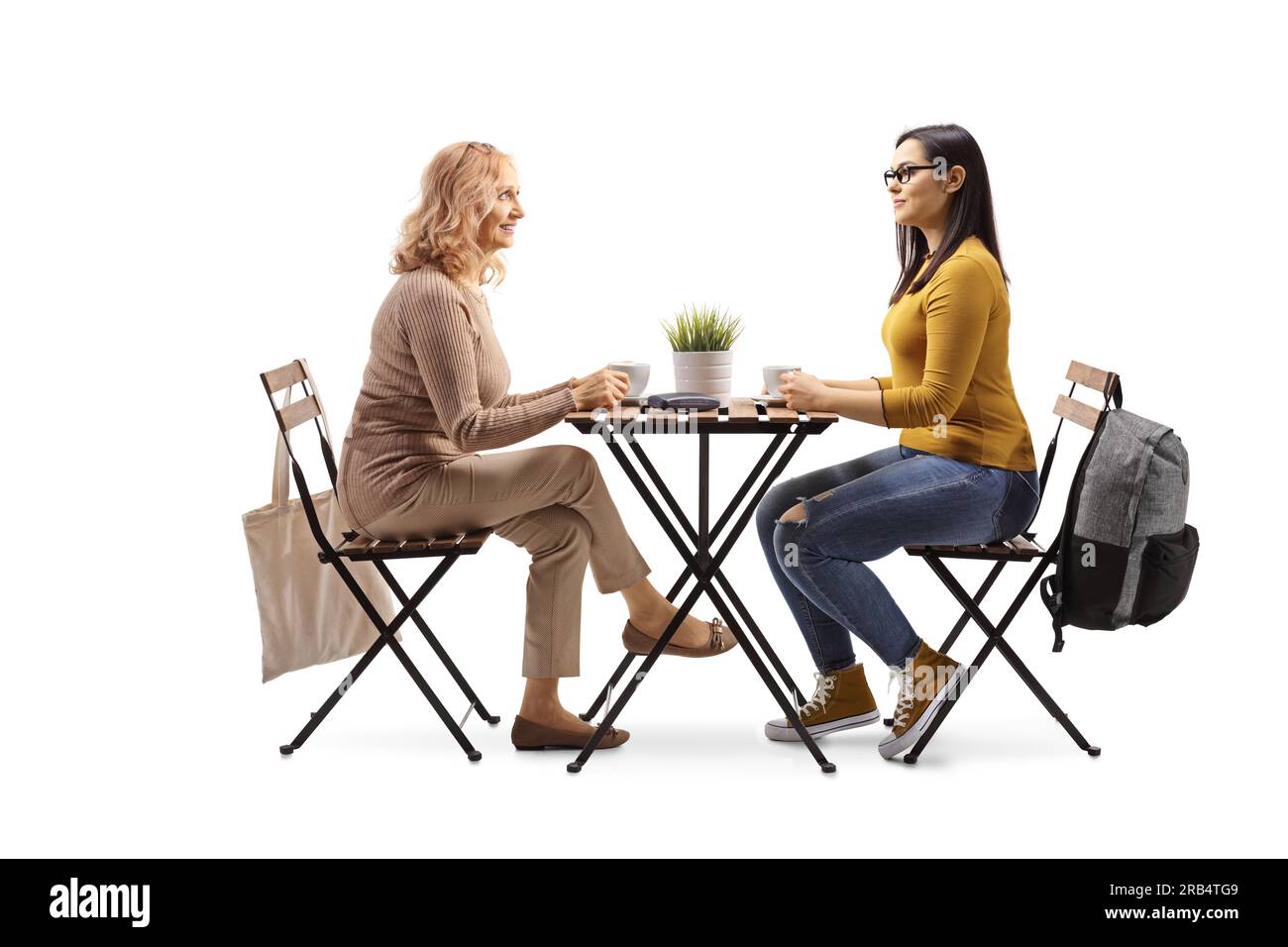 Reife und jüngere Frau, die an einem Tisch sitzt und eine Tasse Kaffee trinkt, isoliert auf weißem Hintergrund Stockfoto