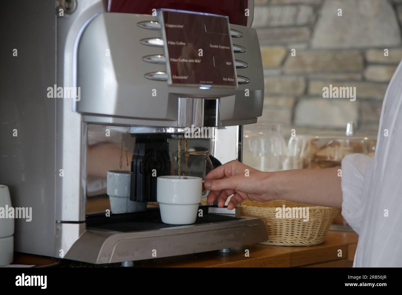 Frau, die Kaffee mit der Kaffeemaschine in der Selbstbedienungs-Cafeteria macht Stockfoto
