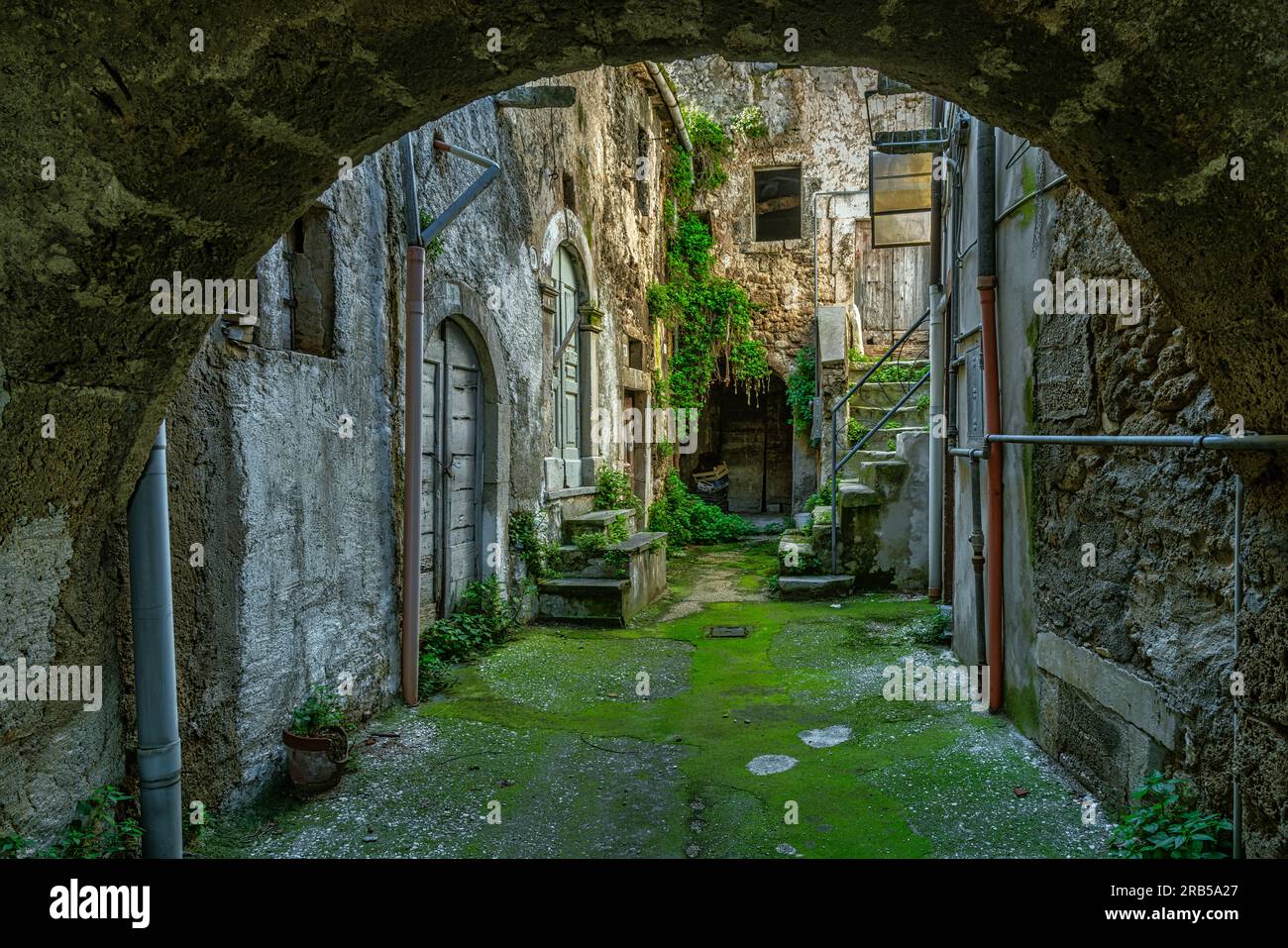 Innenhof mit Bogeneingang mit Moos auf dem Boden und Steinhäusern im mittelalterlichen Dorf Tocco da Casauria. Tocco da Casauria, Abruzzen Stockfoto