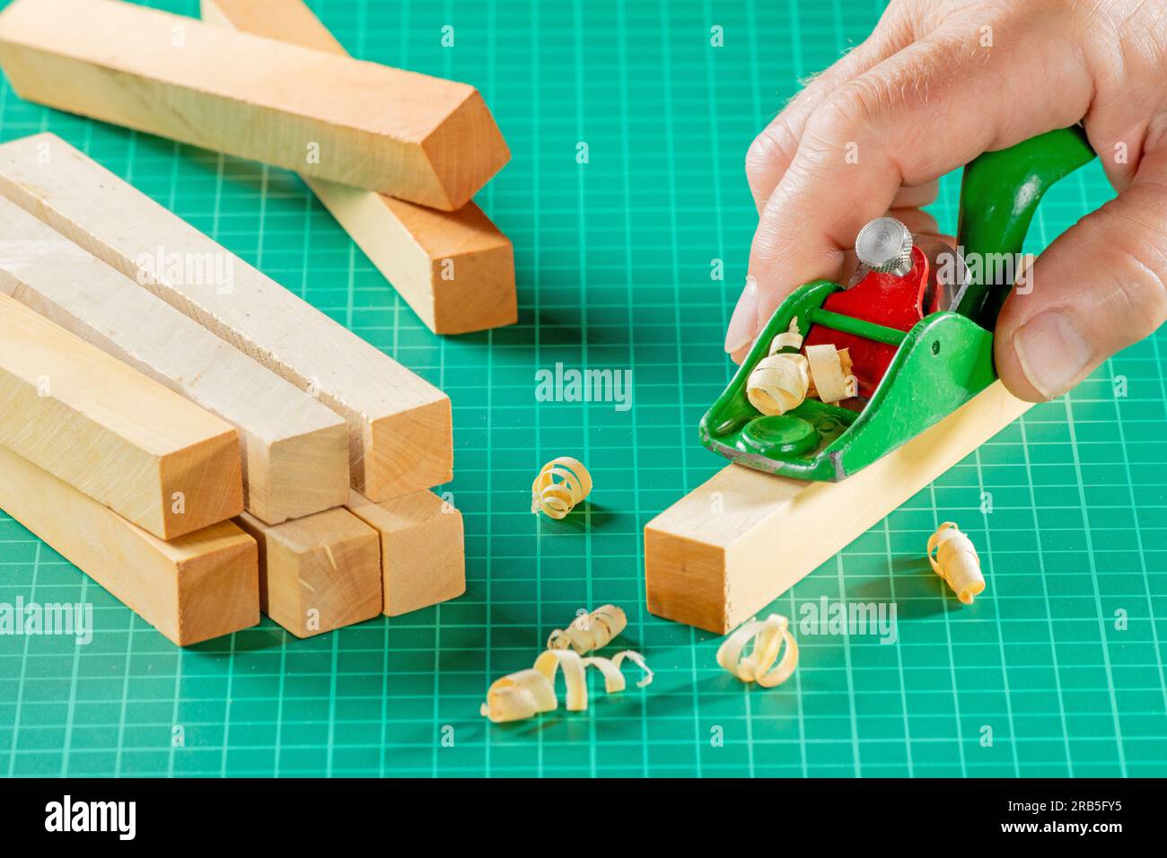 Die Hand des Modellierers schneidet mit einem Miniplaner auf einem grünen Modelteppich einen Holzblock Stockfoto