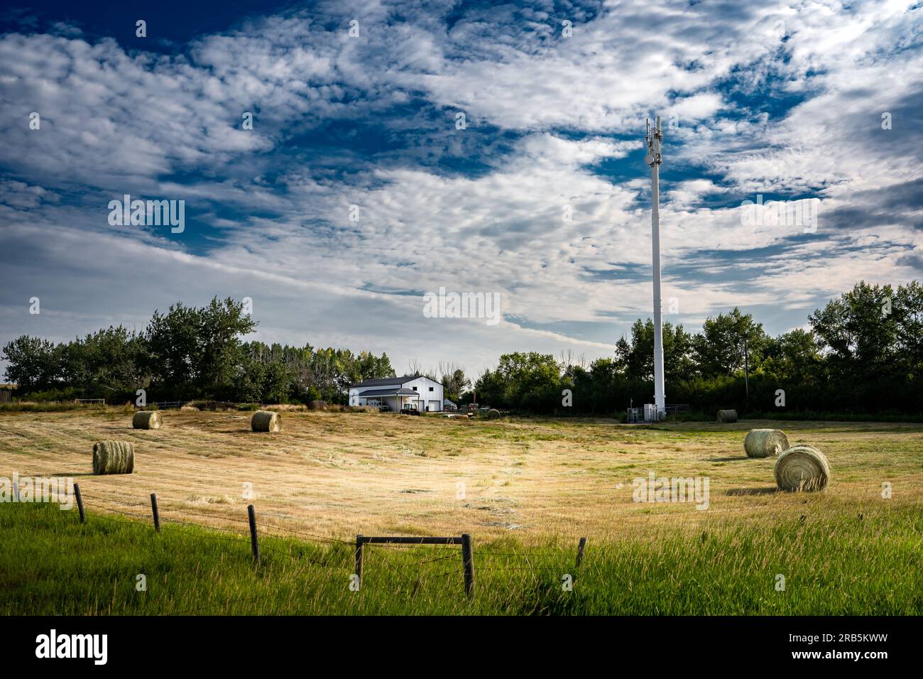 Handyturm mit Blick auf runde Strohballen auf einem kleinen Hof mit Stacheldrahtzaun im Rocky View County Alberta, Kanada. Stockfoto