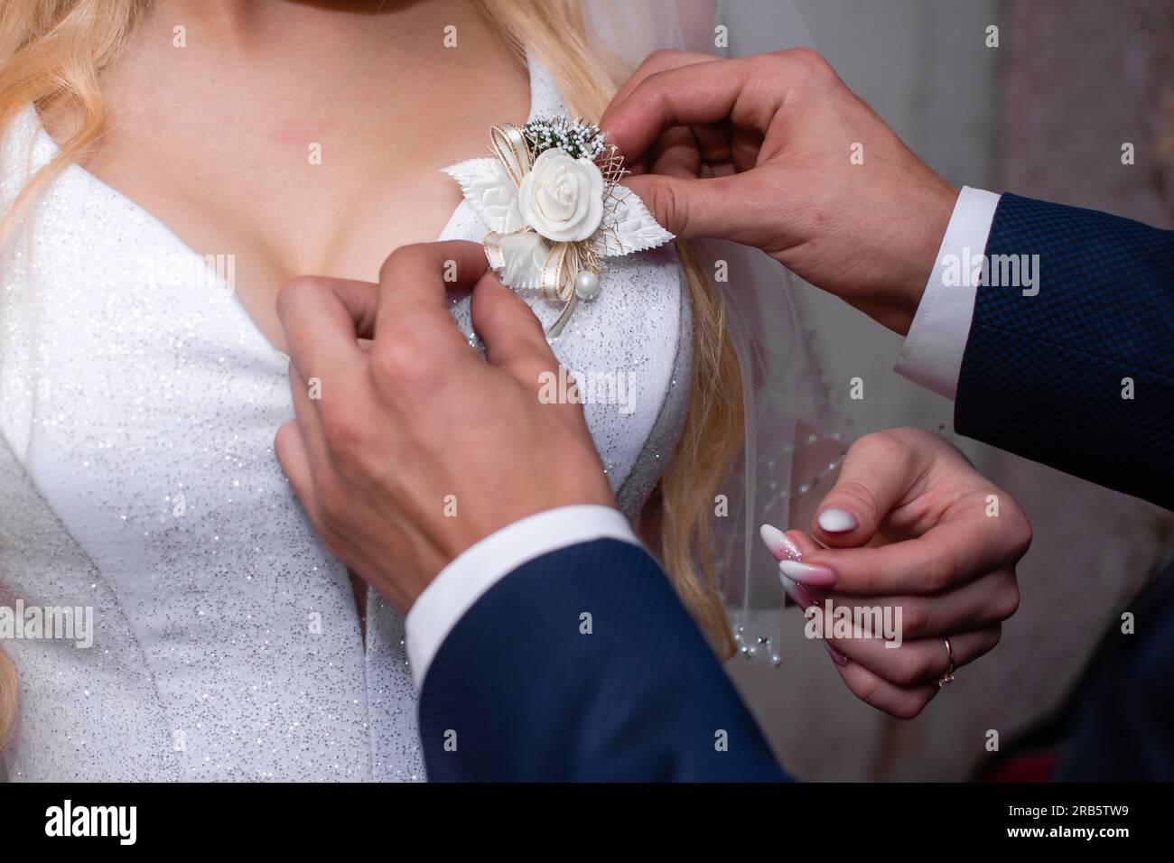 Der Bräutigam passt die Dekoration in Form einer Blume auf dem Brautkleid an. Stockfoto