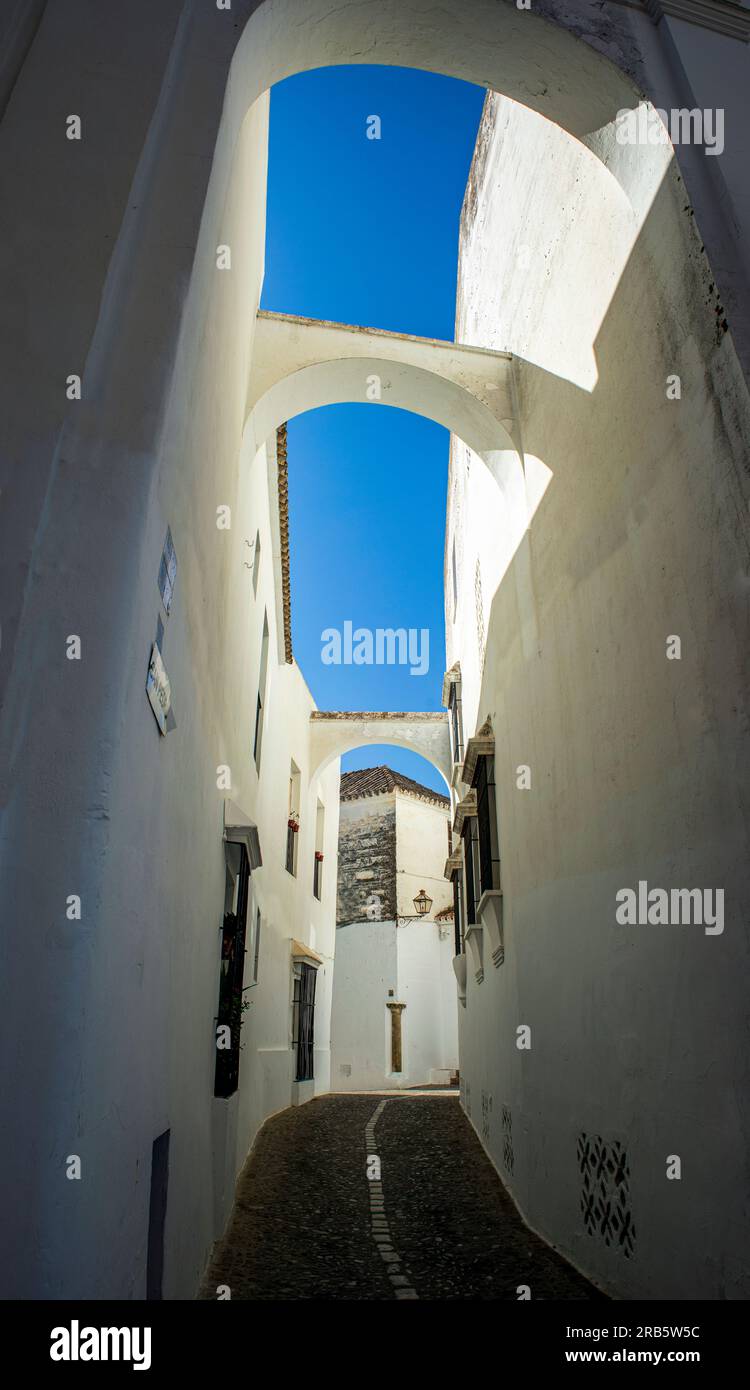 Vertikales Bild einer schmalen weißen Gasse der Altstadt von Arcos de la Frontera, Cadiz, Andalusien, Spanien, mit Bögen zwischen den Häusern und blau Stockfoto