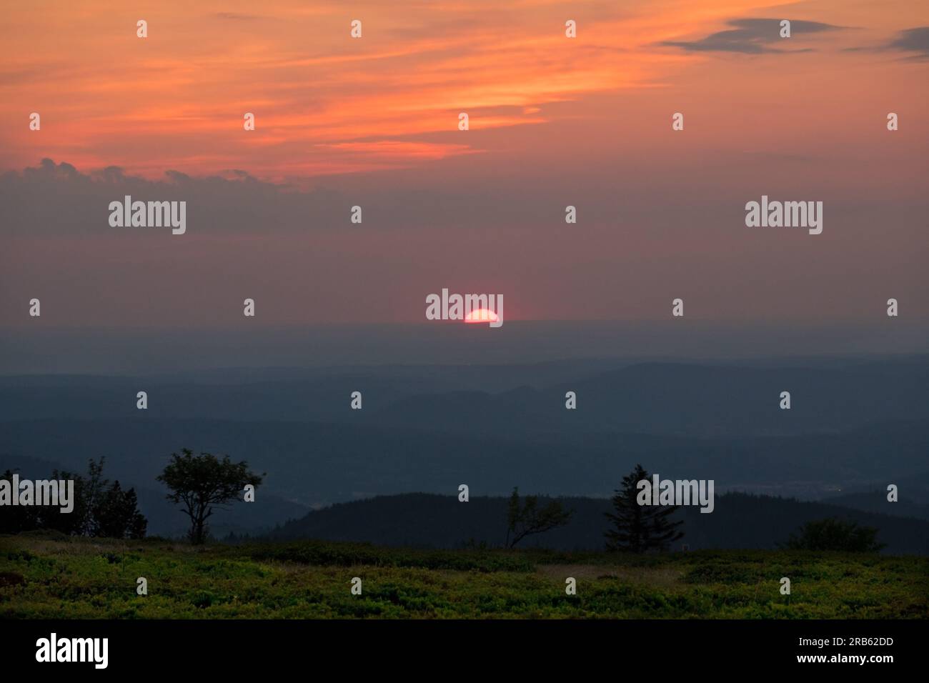 Sonnenuntergang über den Hügeln der Vogesen, orangefarbene Sonne am Abendhimmel, Bergketten in der Ferne verblassen Stockfoto
