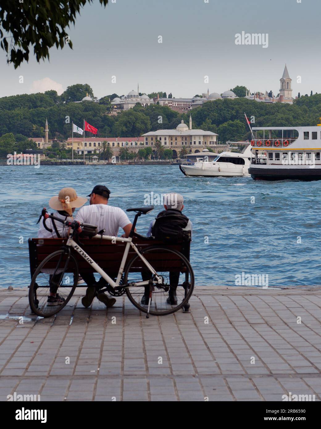 Ein Paar und ein älterer Mann sitzen an einem Sommerabend auf einer Bank in Karakoy mit Blick auf das Goldene Horn und den Topkapi-Palast, Istanbul, Türkei Stockfoto