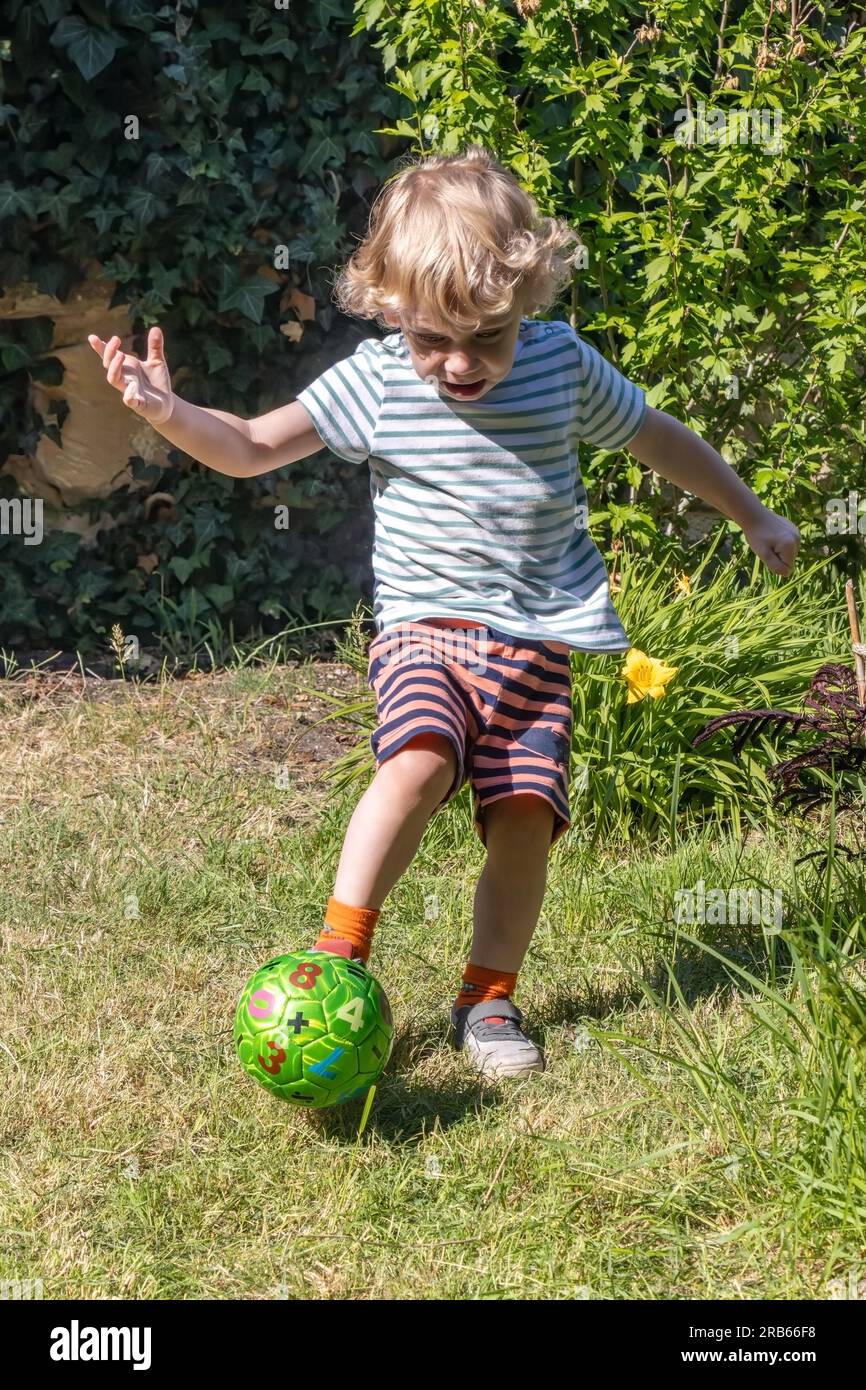 Ein kleiner Junge tritt einen Ball im Sommergarten Stockfoto