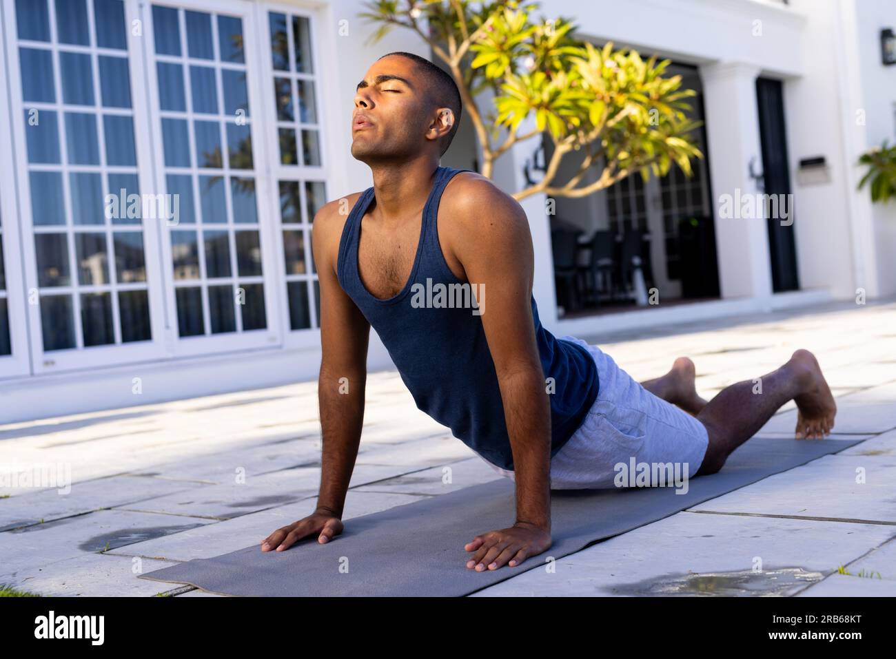 Fokussierter birassistischer Mann, der Yoga im sonnigen Garten praktiziert. Cobra Pose, Sommer, Wohlbefinden, Fitness und gesunder Lebensstil, unverändert. Stockfoto