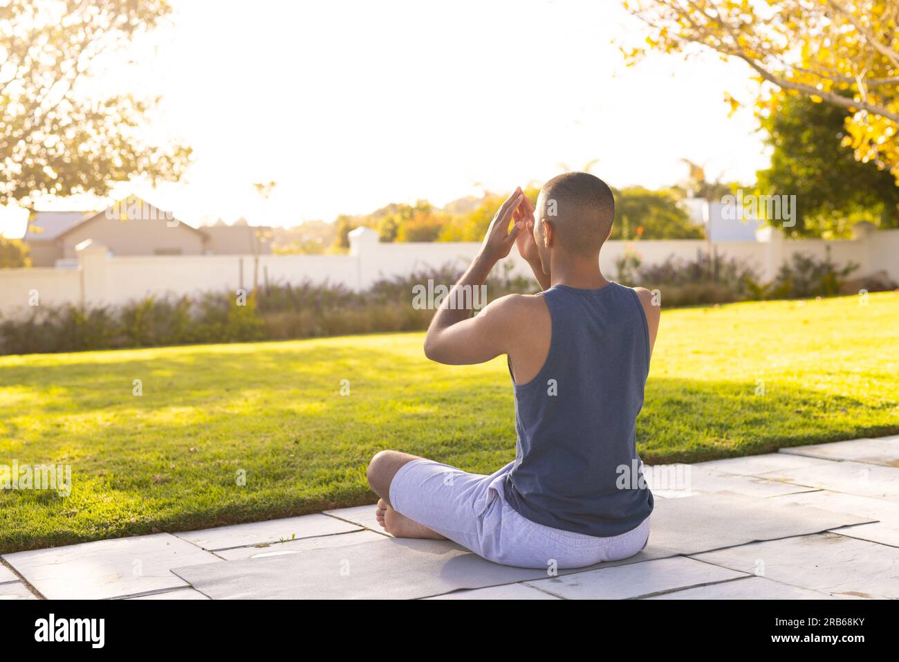 Fokussierter, birassistischer Mann, der Yoga-Meditation praktiziert und im sonnigen Garten sitzt. Sommer, Wohlbefinden, Fitness und gesunder Lebensstil, unverändert. Stockfoto